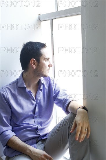 Pensive Caucasian man sitting on windowsill