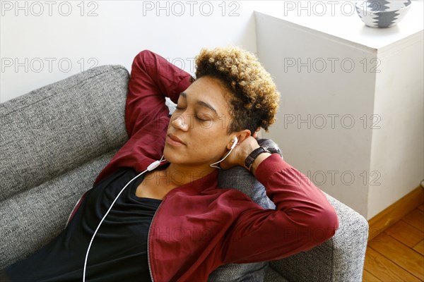 Mixed race woman laying on sofa listening to earbuds