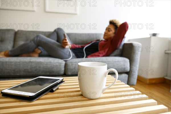 Mixed race woman laying on sofa listening to earbuds