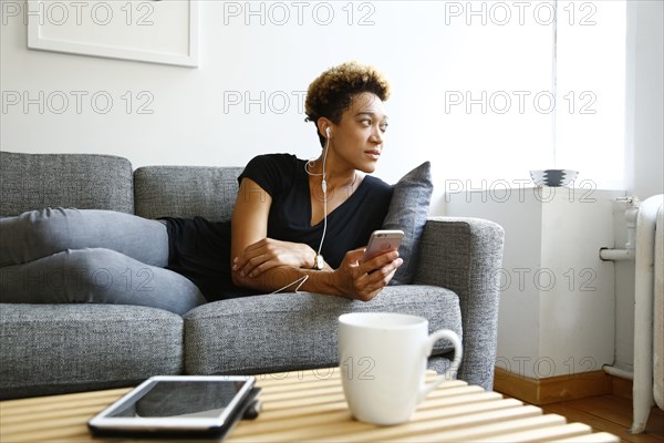 Mixed race woman laying on sofa listening to earbuds