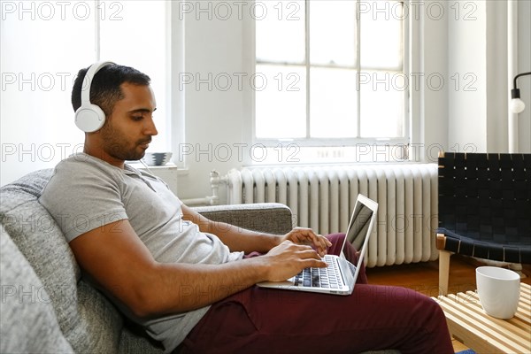 Mixed race man sitting on sofa listening to laptop with headphones