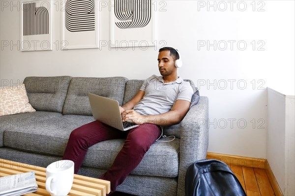 Mixed race man sitting on sofa listening to laptop with headphones