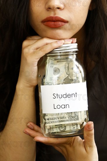 Portrait of mixed race woman holding jar of money for student loan