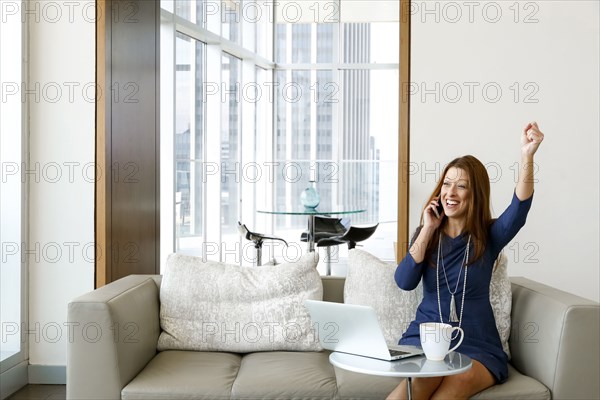 Caucasian businesswoman talking on cell phone and celebrating