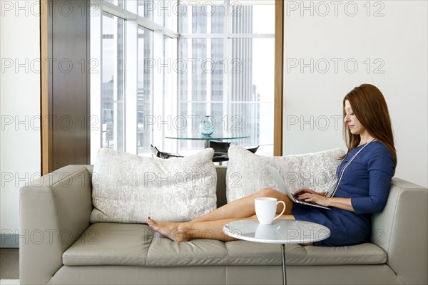 Caucasian businesswoman relaxing on sofa using laptop
