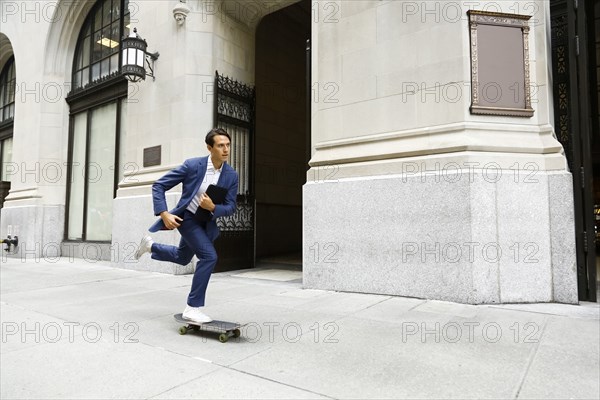 Caucasian businessman skateboarding on urban sidewalk