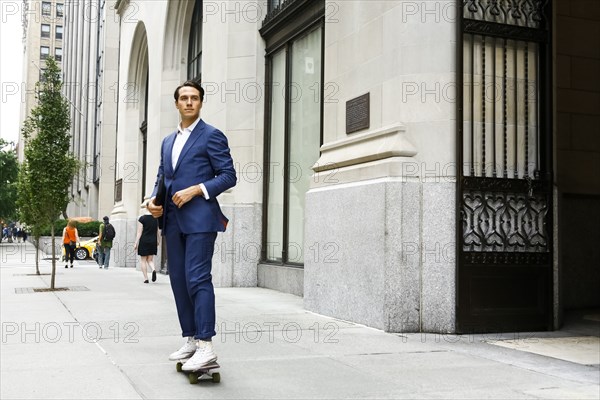 Caucasian businessman skateboarding on urban sidewalk