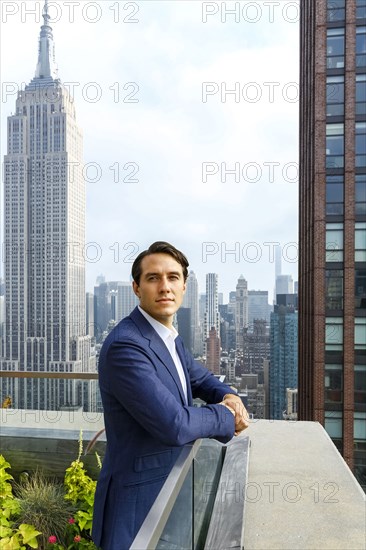 Portrait of serious Caucasian businessman leaning on urban rooftop