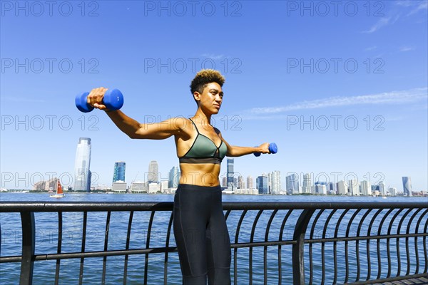 Mixed race woman lifting dumbbells at waterfront