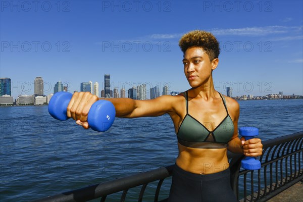 Mixed race woman lifting dumbbells at waterfront