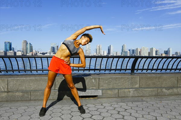 Mixed race woman stretching arm at waterfront
