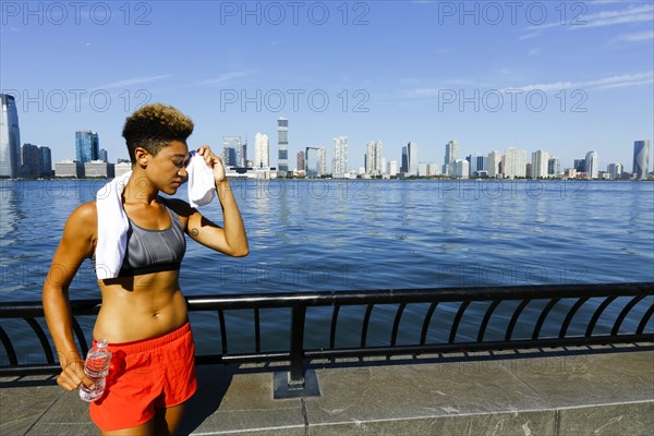 Mixed race woman wiping forehead with towel at waterfront