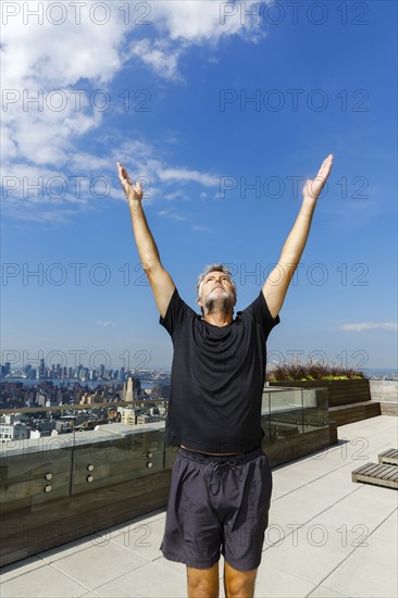 Caucasian man standing with arms raised on urban rooftop