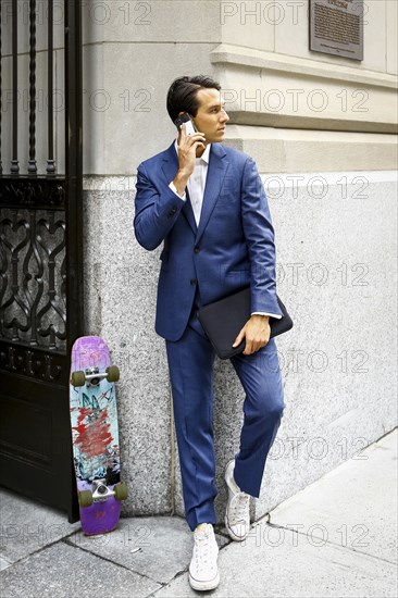 Caucasian businessman with skateboard talking on cell phone