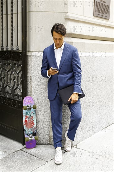 Caucasian businessman with skateboard texting on cell phone