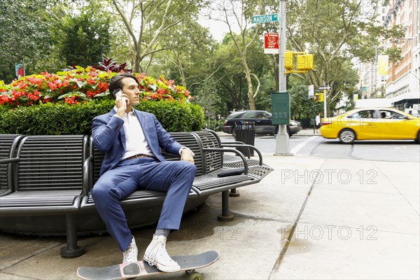 Caucasian businessman sitting on bench in city talking on cell phone