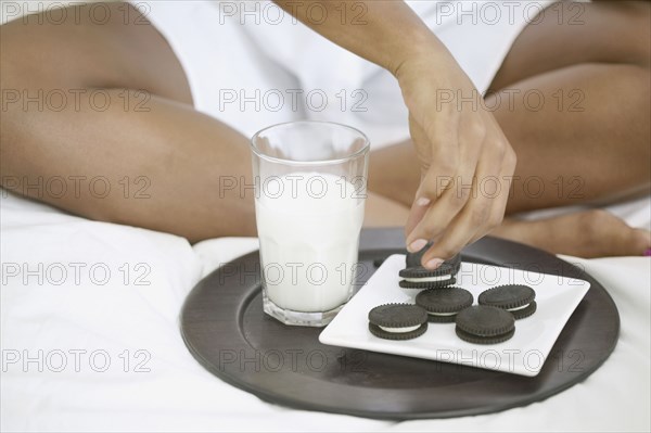 Low section of woman sitting on bed with milk and cookies