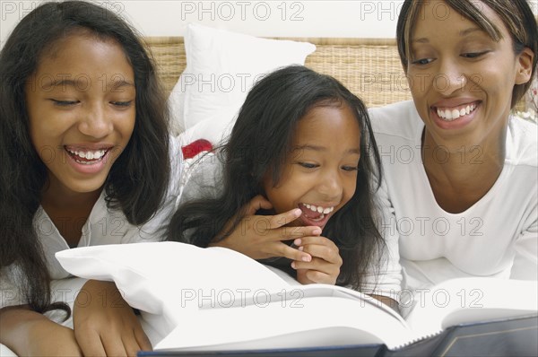 African American mother and daughters on bed with book