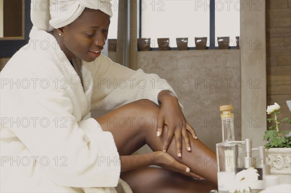 African American woman in bathrobe applying lotion