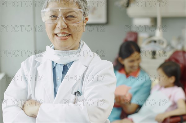 Senior Asian female dentist with assistant and patient in background