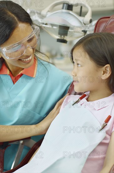 Indian female dental assistant smiling at young Asian female patient