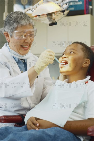 Senior Asian female dentist and African boy in dentist's chair