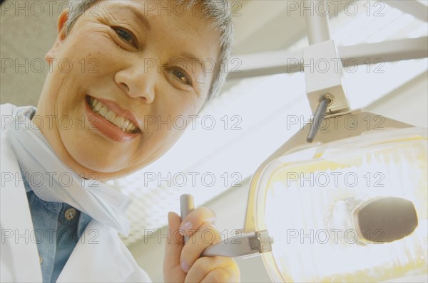 Senior Asian female dentist adjusting light