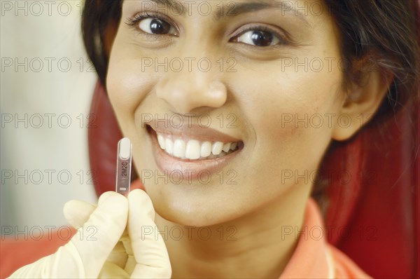 Tooth color sample being held up next to Indian woman's teeth