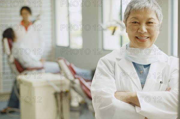 Senior Asian female dentist with assistant and patient in background