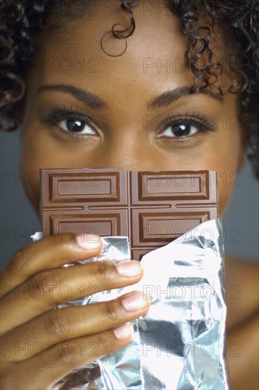 African woman holding chocolate bar in front of face