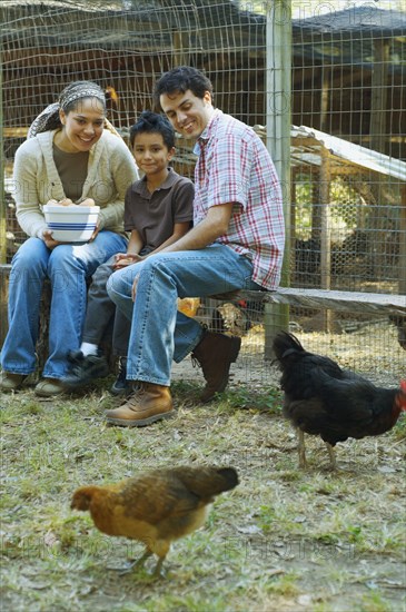 Multi-ethnic family holding bowl of eggs next to chickens