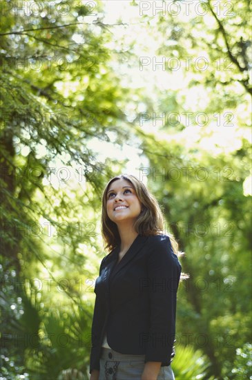 Hispanic businesswoman looking up in woods