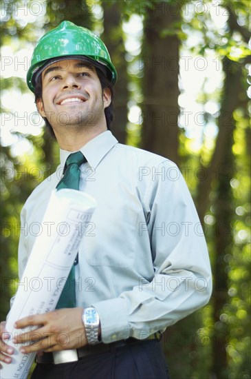 Hispanic architect holding blueprint and wearing green hard hat