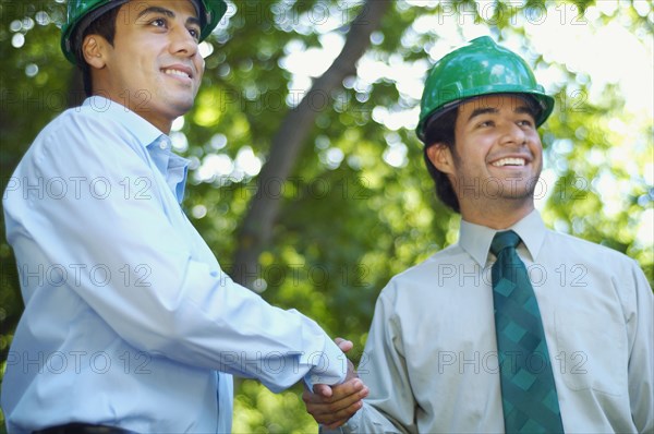 Hispanic businessmen in green hard hats shaking hands outdoors