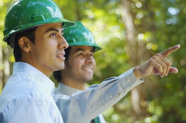 Hispanic businessmen in green hard hats pointing outdoors