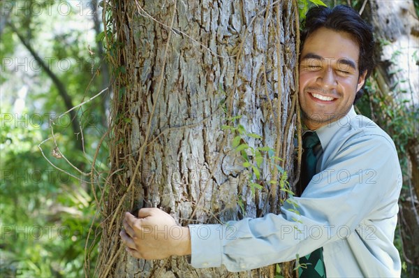 Hispanic businessman hugging tree