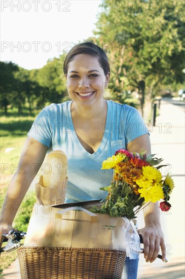 Mixed race woman riding bicycle with flowers in basket