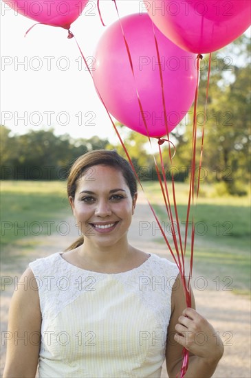 Mixed race woman with pink balloons in park