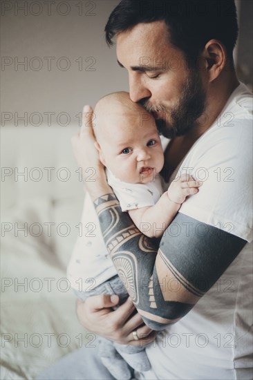 Caucasian father with tattoos on arms kissing baby son