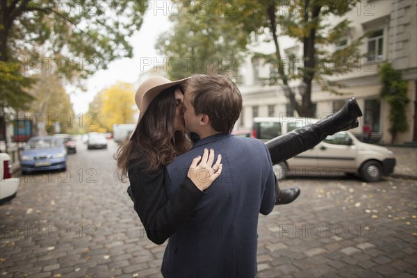 Caucasian man carrying and kissing woman on cobblestone street