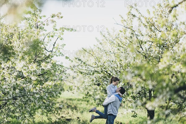 Caucasian man lifting woman under flowering trees