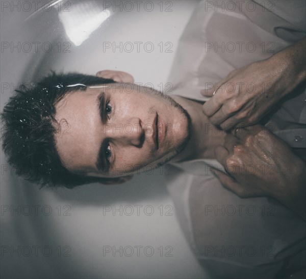 Caucasian man wearing shirt laying underwater in bathtub