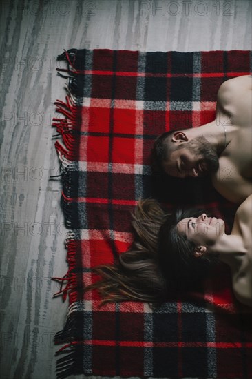 Caucasian couple laying face to face on plaid blanket