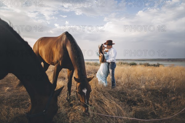 Horses grazing near Caucasian woman hugging cowboy