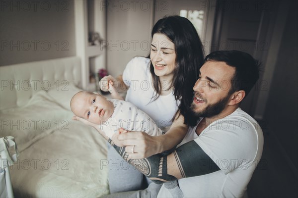 Caucasian mother and father on bed playing with baby son