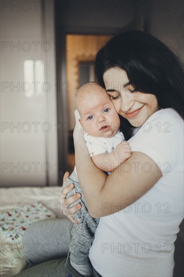 Caucasian mother kneeling on bed hugging baby son