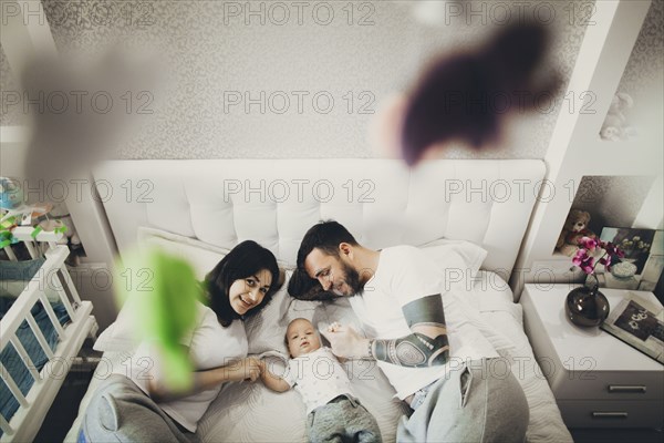 Caucasian mother and father holding hands with baby son on bed