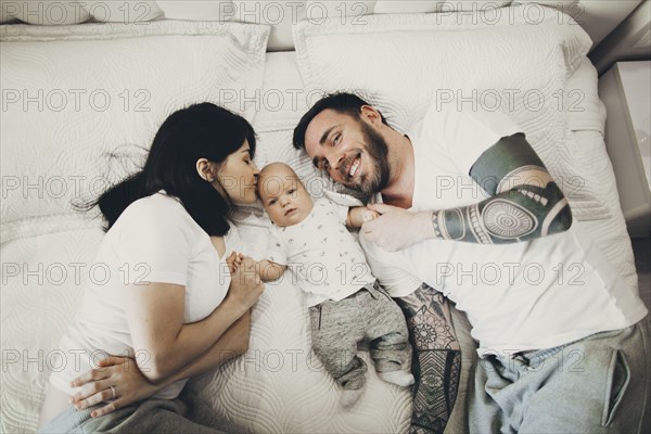 Caucasian mother and father holding hands with baby son on bed