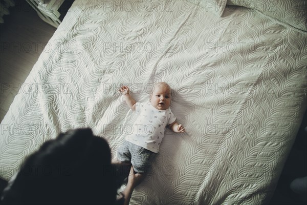 Caucasian mother holding legs of baby son on bed