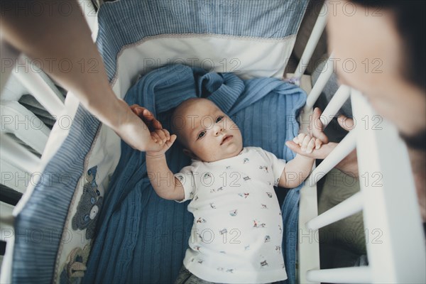 Caucasian mother and father holding hands of baby son in crib